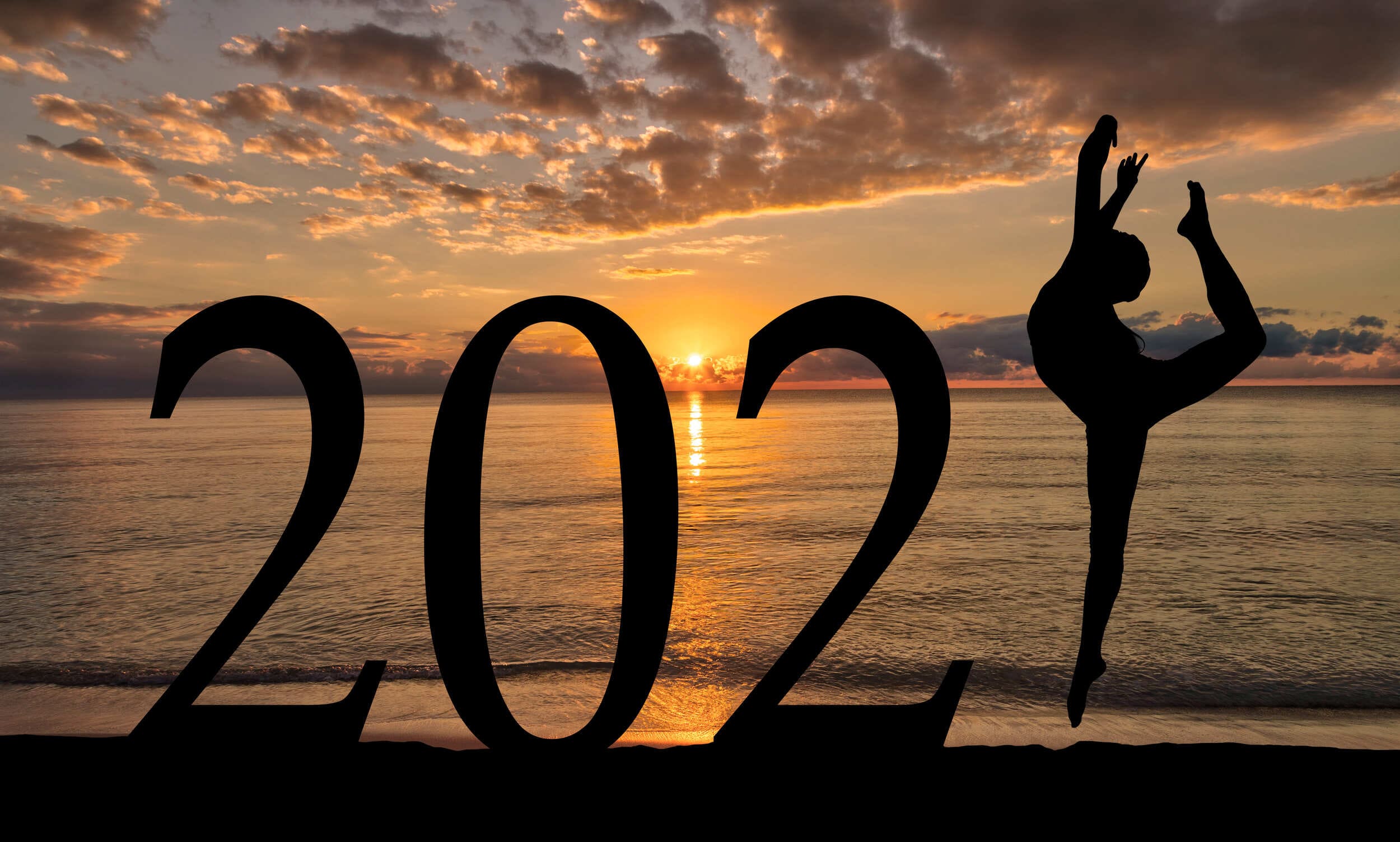 Silhouette of a person performing a yoga pose forming part of the number '2021' against a beautiful sunset on the beach.