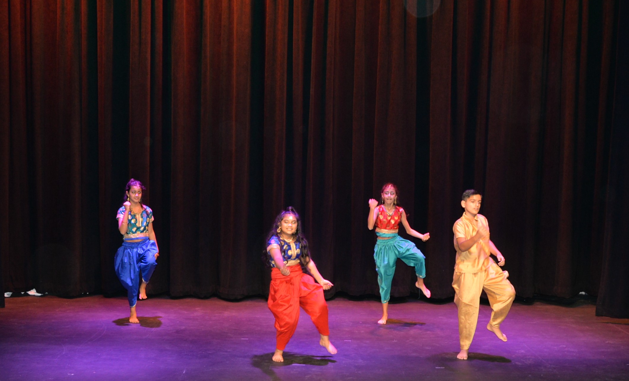 Dance Expression students showcasing their dance skills at the 2021 Dance Expression showcase, performing on stage in colourful traditional attire against a red curtain backdrop.