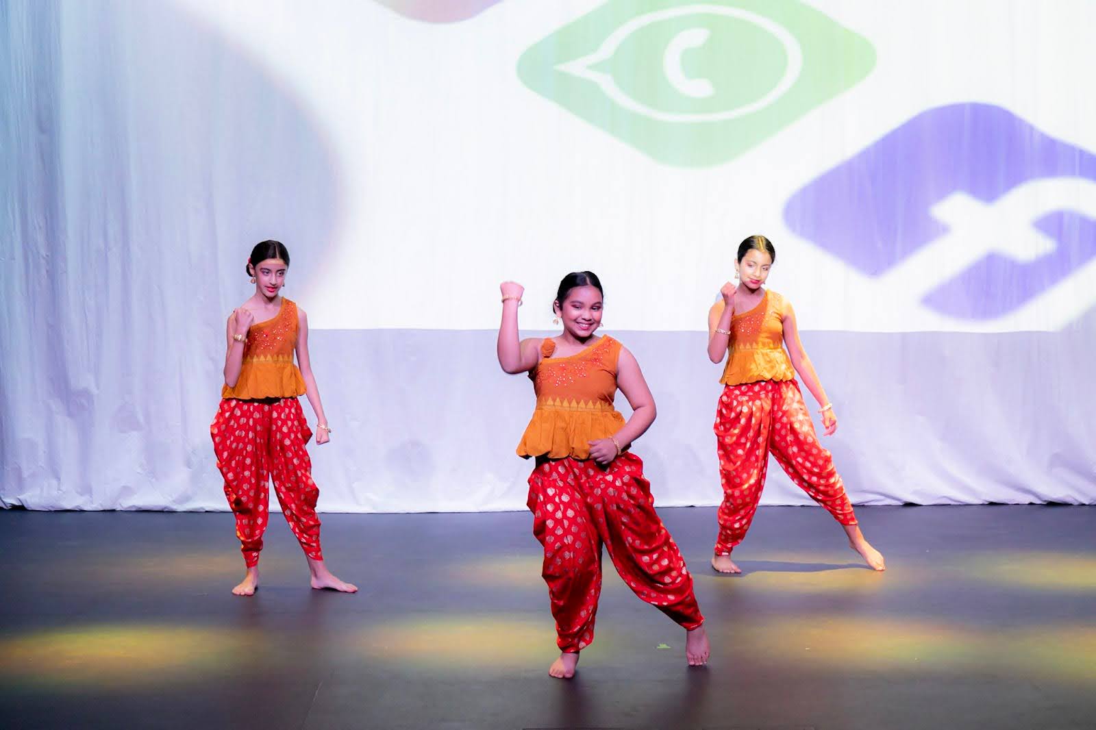 Stephanie Persaud takes center stage at the Dance Expression Summer Showcase 2022, confidently performing with fellow dancers in vibrant red and orange traditional attire.