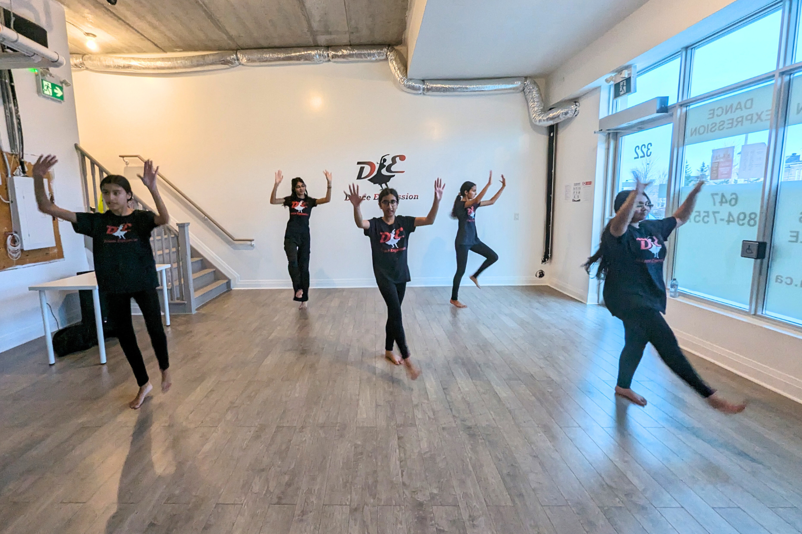Tweens and teens participating in a Bhangra class at Dance Expression Studio, performing a dance sequence in unison while wearing the studio's DE logo t-shirts.